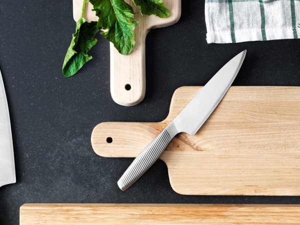 Coltello da cucina IKEA 365+ in acciaio inossidabile appoggiato su un tagliere in legno accanto ad altri due taglieri in legno - IKEA.