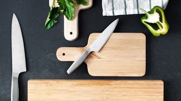 Coltello da cucina in acciaio inossidabile sopra a un tagliere in legno, con accanto un coltello da cucina più grande - IKEA