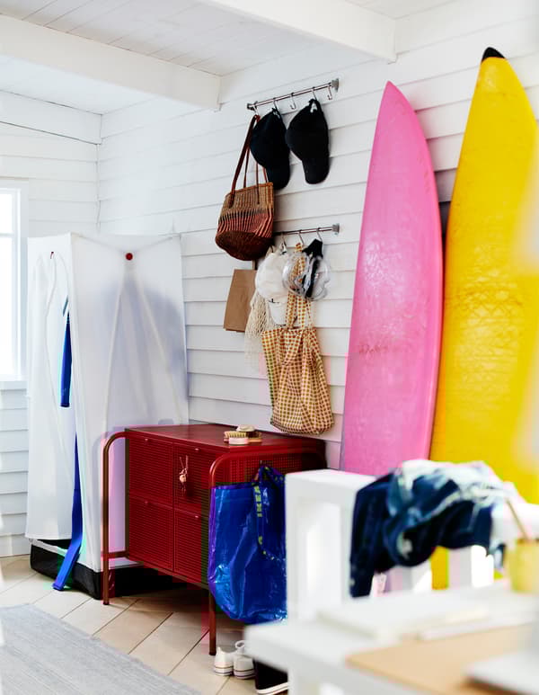 Colțul unei încăperi cu lambriu alb, cu un dulap VUKU, o comodă NIKKEBY și sertare și plăci de surf sprijinite de perete.