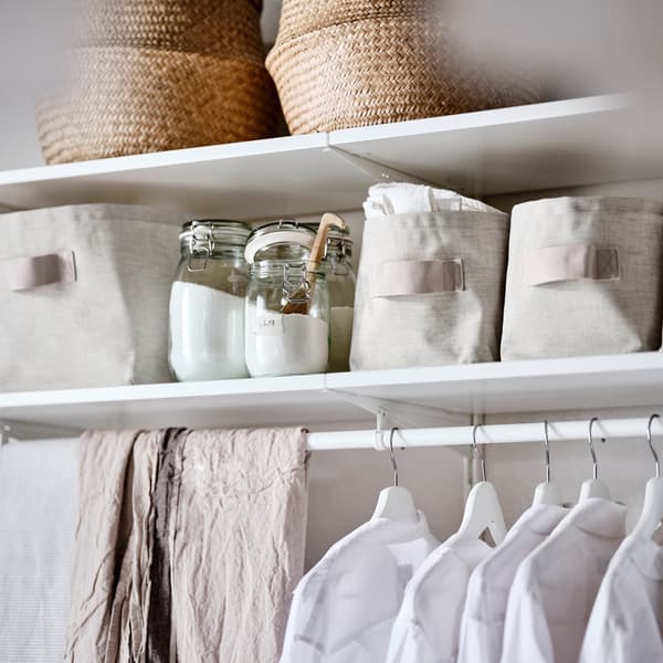 Combinação de roupeiro em branco com cestos feitos de alga, cestos de arrumação em tecido bege e roupa pendurada em cabides em branco.