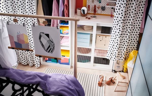 Combinación de almacenamento aberto e pechado ao longo dunha parede, cun corredor que se forma entre as cortinas colgadas na fronte e un extremo da cama.