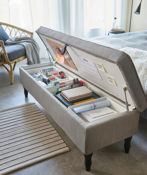 Combinaison banquette/rangement revêtue de textile. Installée au pied du lit, elle dévoile différents objets destinés à un travail de bureau à domicile.