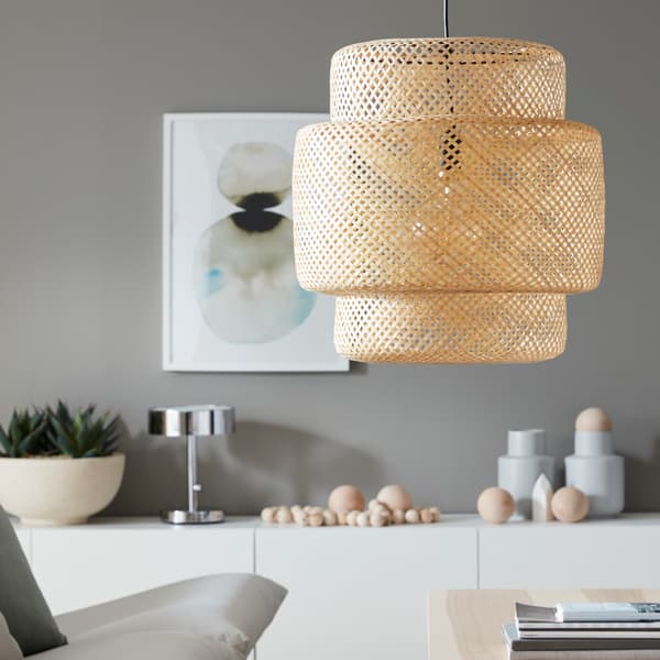 Comedor con mesa de madera y patas de fierro, con dos sillas a su alrededor. Se ve la lampara hecha de material sustentable y perteneciente a la familia SINNERLIG de IKEA. De fondo tenemos el producto icónico de la marca en la foto que es conocido como METOD, en este caso color gris.