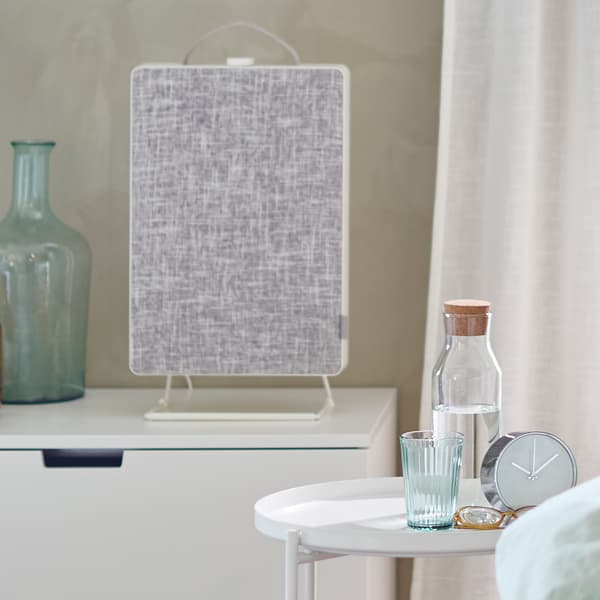 Commode sur laquelle sont posés un purificateur d’air FÖRNUFTIG et un vase, à côté d’une petite table et d’un rideau.