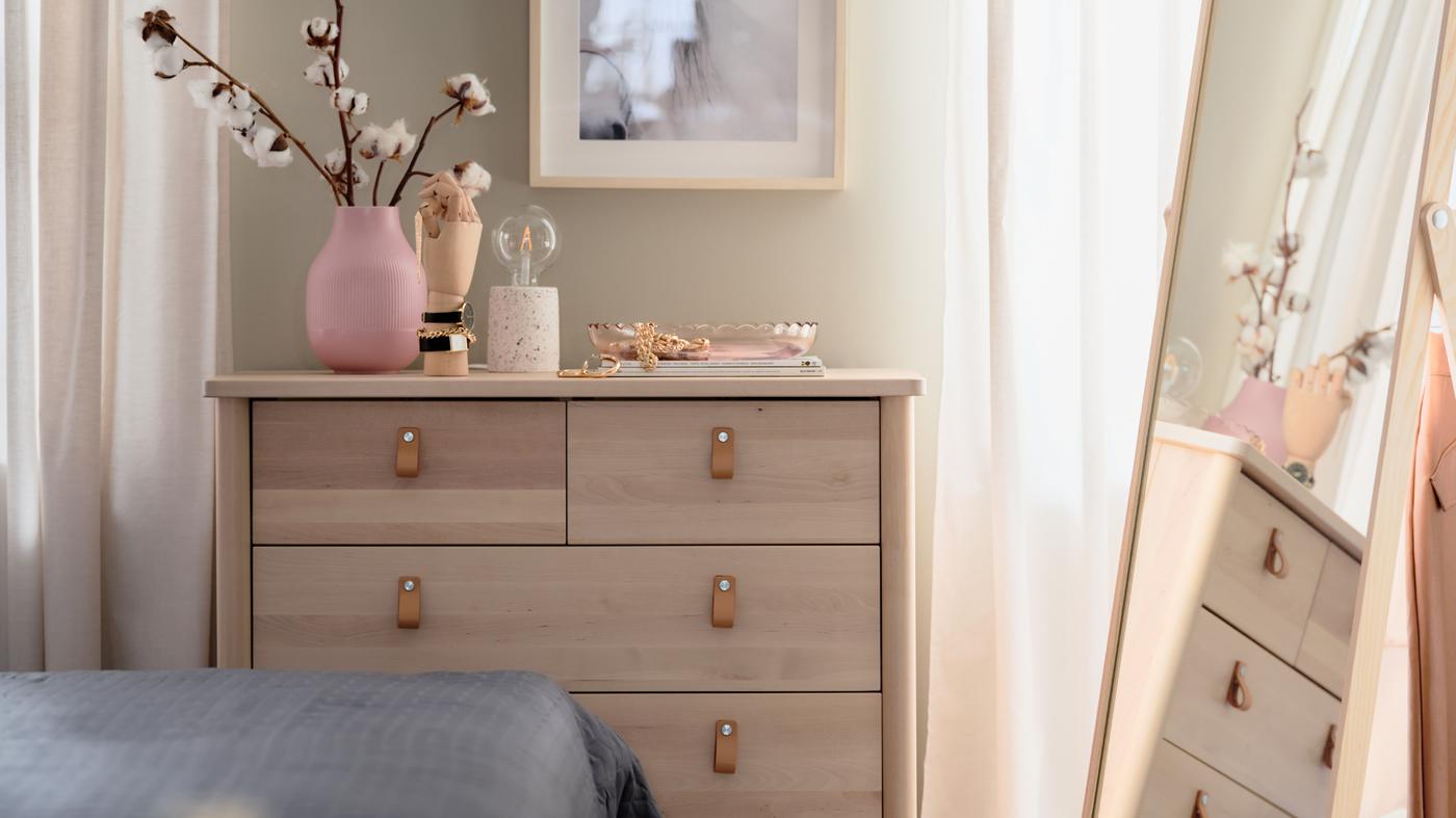 Cómoda com 5 gavetas BJÖRKSNÄS em bétula, com artigos decorativos em cima e um quadro pendurado por cima, num quarto.