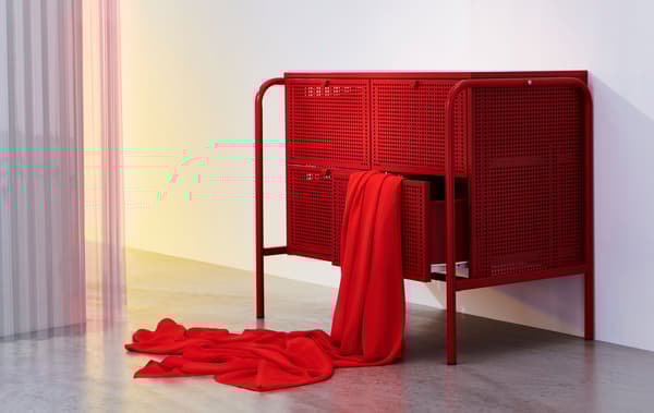 Cómoda metálica em vermelho com quatro gavetas, com um pano vermelho pendurado artisticamente para fora de uma gaveta.