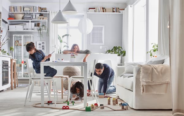 Compact-living home where a family plays with a LILLABO train set in a room with bed, sofa, table, kitchenette, and storage.