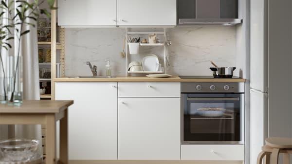 Compact white KNOXHULT kitchen with wooden countertop, built-in oven and hob, marble-look backsplash, open shelves and soft natural light.