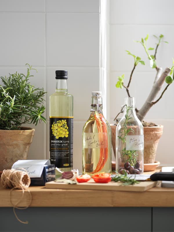 Comptoir de cuisine avec des plantes en pot et deux bouteilles en verre KORKEN utilisées pour infuser de l’huile de colza avec des épices et des fines herbes.