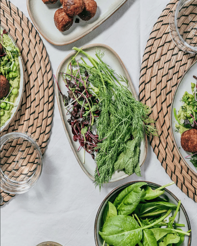 Conjunto de hierbas dispuestas sobre un plato GLADELIG sobre una mesa  con mantel blanco e individuales redondos. 