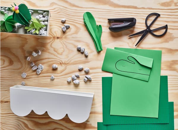Construction paper, scissors, pebbles and a plant pot lay on a wooden surface.