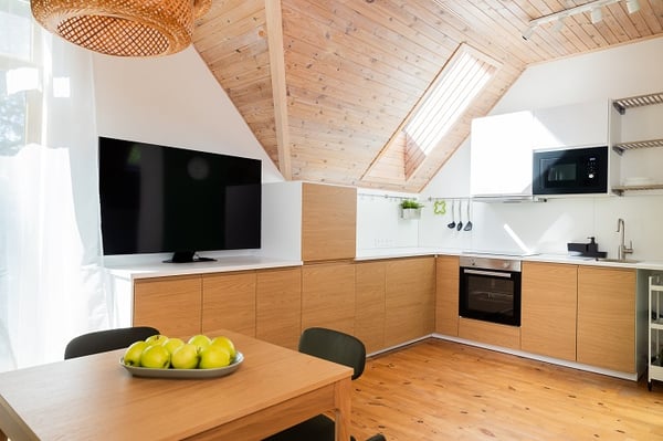 Contemporary attic kitchen with wooden cabinetry, dining table, and natural light
