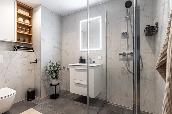 Contemporary bathroom with marble tiles, shower, vanity unit, and LED mirror.