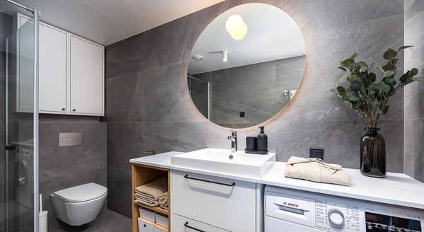 Contemporary bathroom with round mirror, sink and grey tile walls