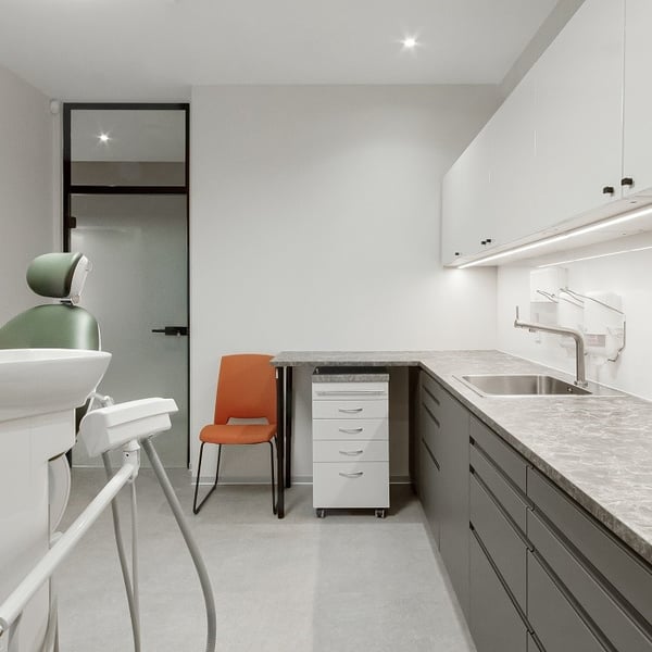 Contemporary dental office with green dentist chair, marble countertop cabinets, and an orange chair against a clean white wall.