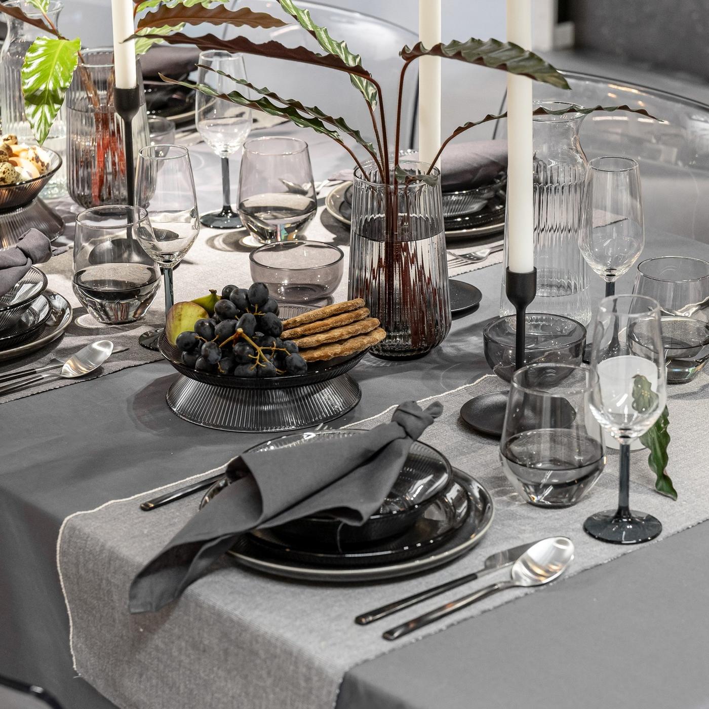 Contemporary dining table styled in muted tones with layered table linens, dark dinnerware and soft candlelight.