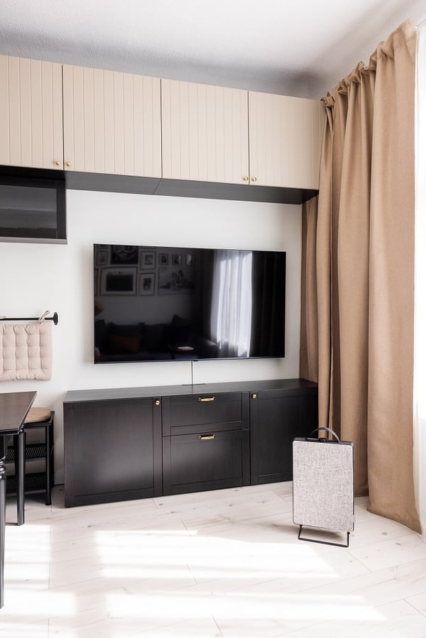 Contemporary living and dining area with wall-mounted TV, storage cabinets, and natural light