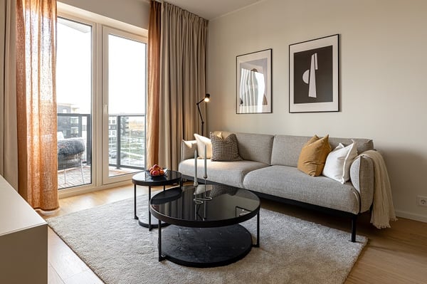 Contemporary living room with gray sofa, coffee tables, and framed wall art near balcony.