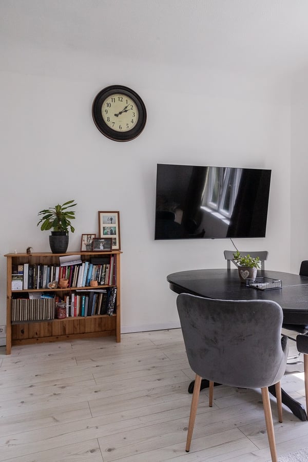 Contemporary living space with dining table, bookshelf, wall clock, and flat-screen TV