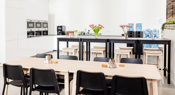 Contemporary office kitchen with high tables, water dispensers, and fresh flower arrangements.