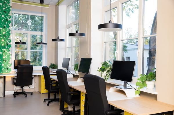 Contemporary office workspace with desks, monitors and pendant lighting by large windows