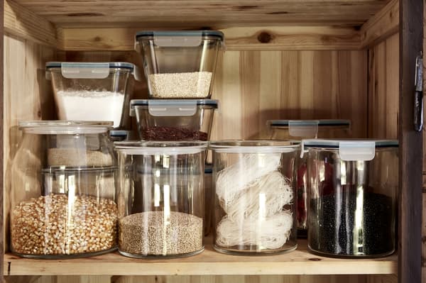 Contenedores de vidrio IKEA 365+ rellenos con frijoles, arroz y especias en una despensa abierta por una mano.