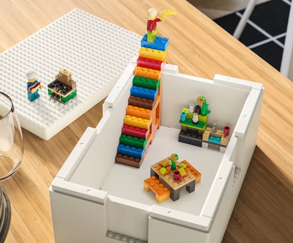 Contenitore BYGGLEK bianco su un tavolo. All’interno, costruzioni realizzate con mattoncini LEGO colorati, tra cui una rampa di scale.
