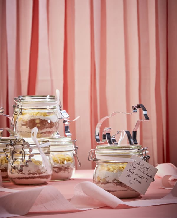 Cookie dough ingredients are layered in glass jars, with a handwritten note and cookie cutter attached.