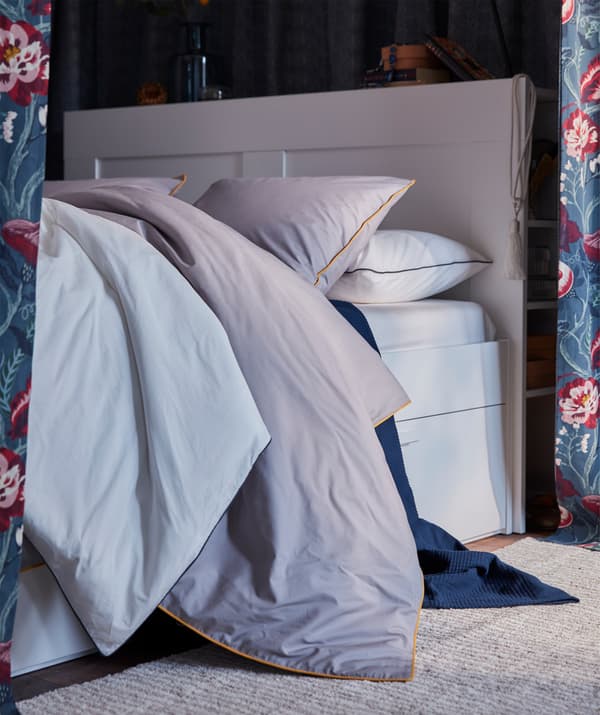 Copripiumino KUNGSBLOMMA grigio con profili gialli su un morbido letto.