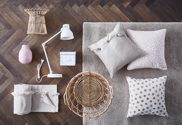Corbeilles en osier, coussins et jeté de couleurs claires, et lampe de travail blanche, le tout exposé sur un plancher de bois.