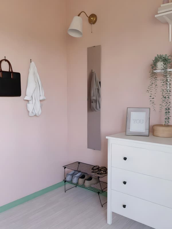 Corner with a white three-drawer dresser, mirror with lamp , and two shoe racks.