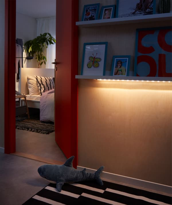Corredor ou espazo fóra dun dormitorio onde unha tira de iluminación LED se ilumina suavemente por baixo do marco dun cadro.