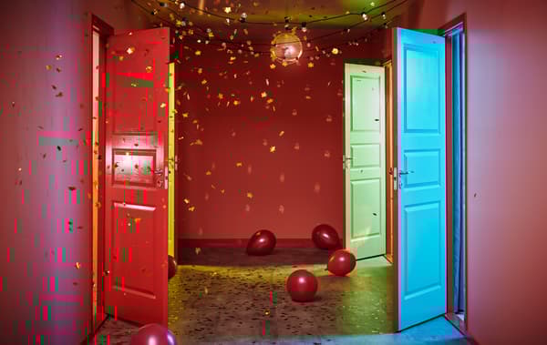 Corridoio decorato per una festa con palloncini per terra e coriandoli dorati in aria. Dalle porte aperte entrano fasci di luce di colori diversi - IKEA