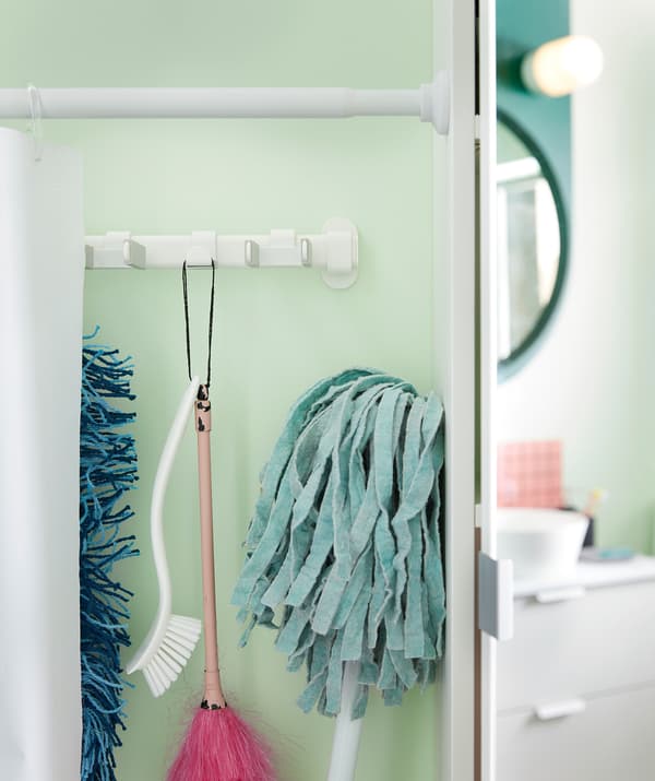 Cortina de duche colocada como divisória ao longo da parede da casa de banho, aberta para o lado para revelar uma fila de equipamento de limpeza pendurado atrás.