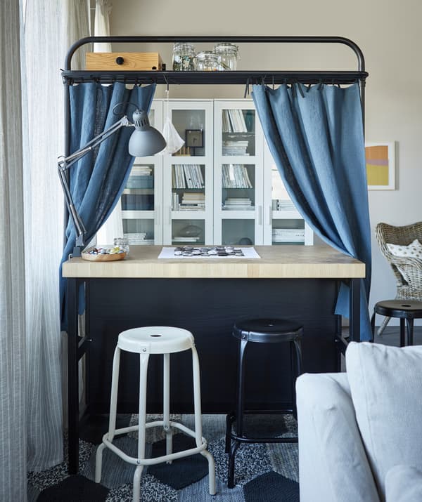 Cortinas azuis colgadas no marco superior nunha illa de cociña, con tallos altos RÅSKOG en fronte.