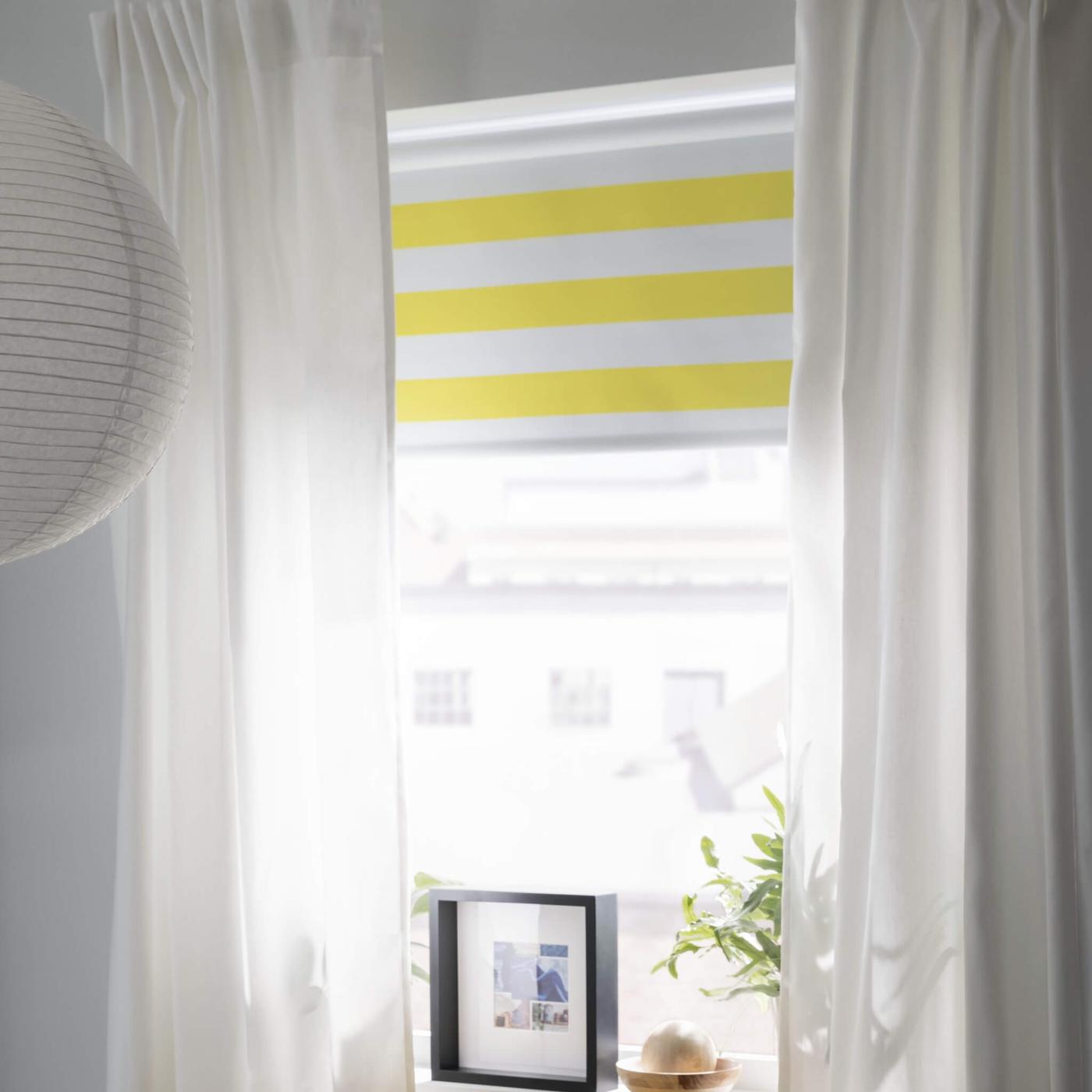 Cortinas blancas y una persiana a rayas de color blanco y amarillo que cubren una ventana luminosa.