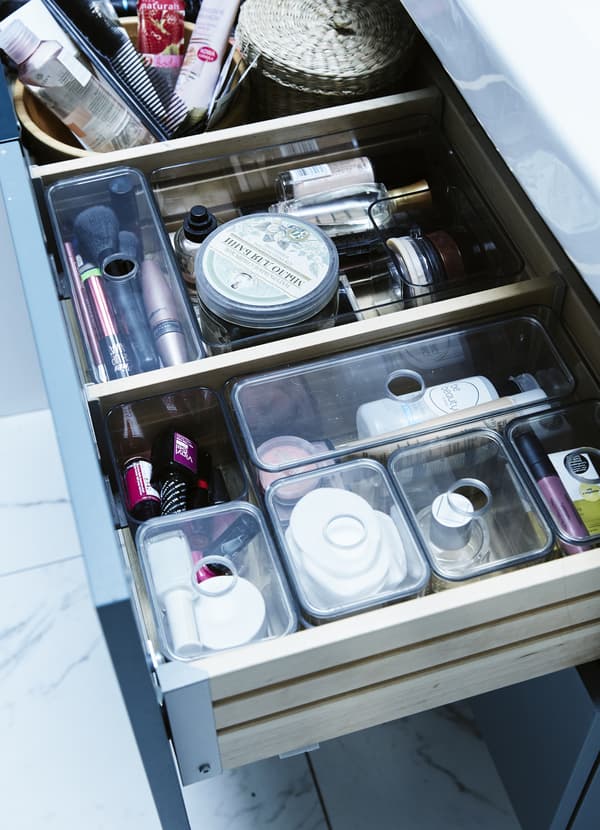 Cosmetics and toiletries organised in tray inserts and boxes inside a bathroom drawer.