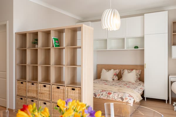 Cosy sleeping area with a double bed, separated by a wooden shelf unit with storage baskets.