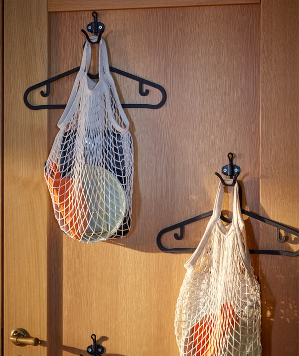 Côté intérieur d’une porte d’entrée en bois, munie de crochets dispersés. Sur chaque crochet, un cintre et un sac en filet contenant un kit de table.