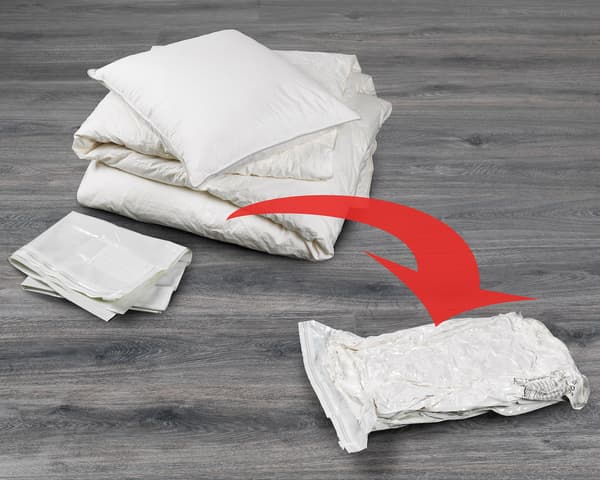 Couette et oreiller posés au sol. Une flèche rouge pointe vers un sac sous vide SPANTAD scellé, montrant ainsi sa capacité.