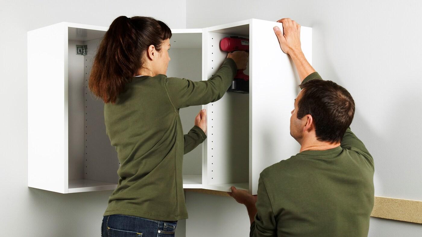 Couple assembling white upper kitchen cabinets together
