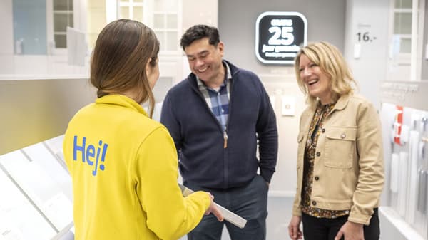 Couple in IKEA kitchen section, employee holding cabinet sample