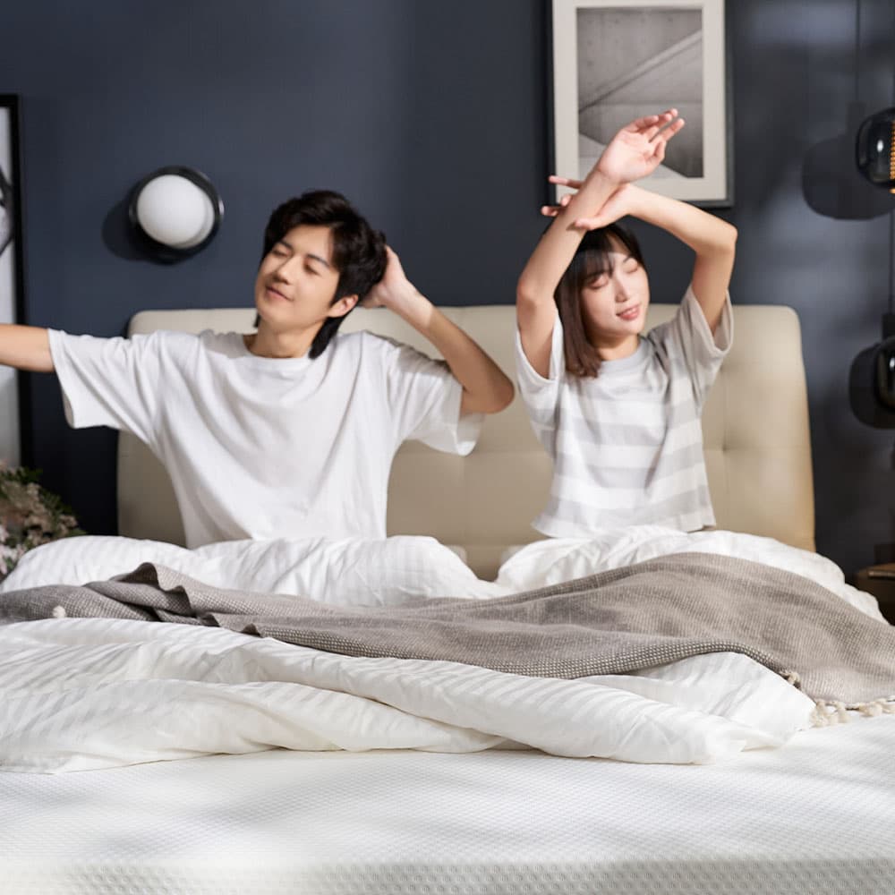 Couple waking up and stretching, looking refreshed on an IKEA mattress.
