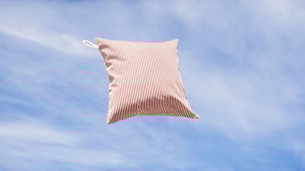 Coussin rayé rouge et blanc avec boucle pour le suspendre, jeté en l’air sous un ciel bleu.