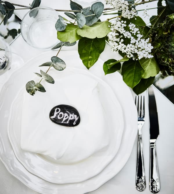 Couvert de table de noces, avec vaisselle blanche, serviette blanche et petit galet peint en guise de marque-place