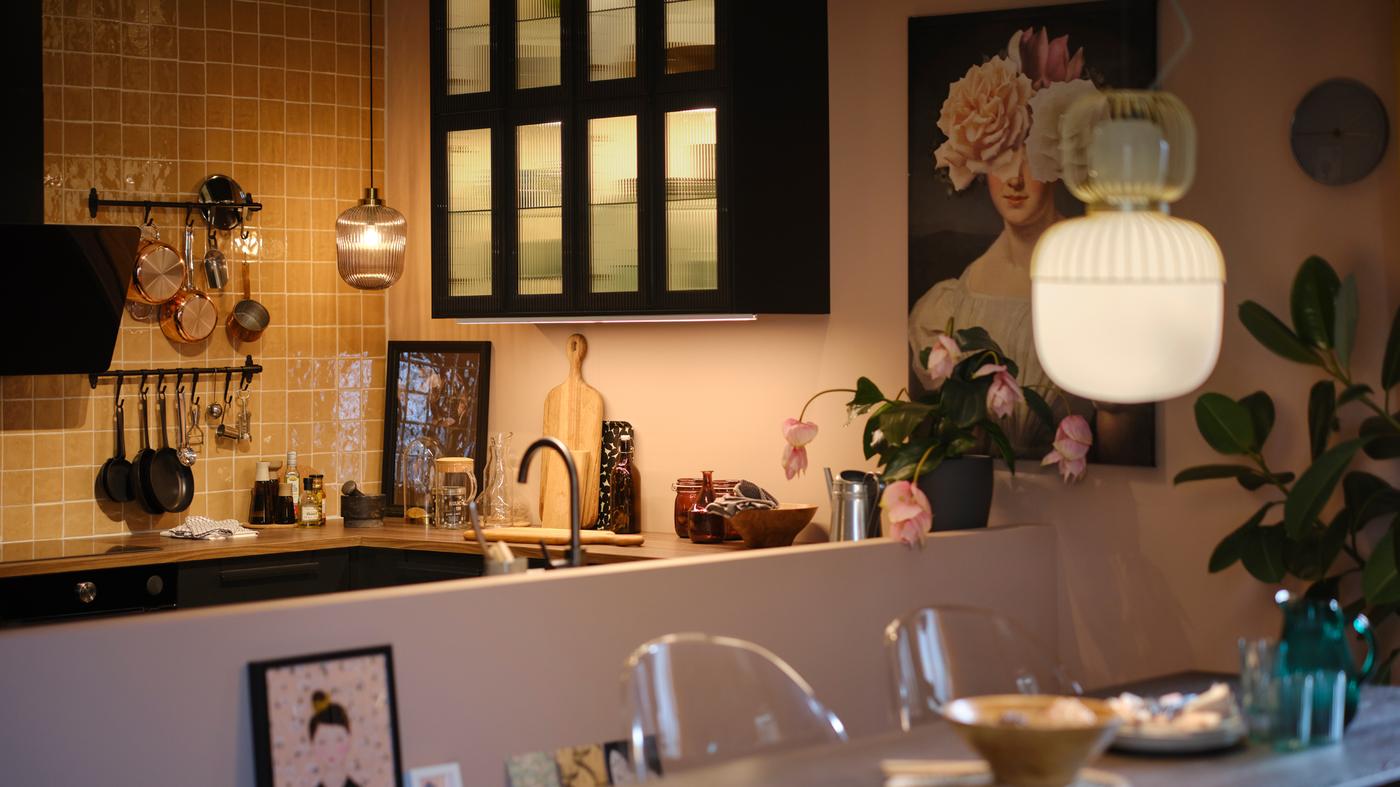 Cozinha com armários de parede com portas de vidro e iluminação no interior, candeeiros suspensos por cima da bancada e mesa extensível.