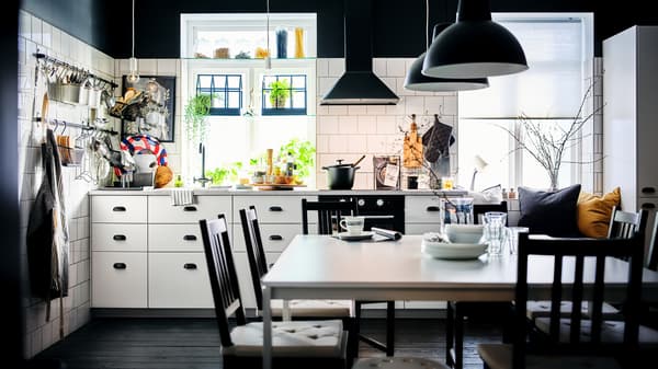 Cozinha em preto e branco com armários METOD em branco com interiores MAXIMERA e espaço de refeição com duas mesas MELLTORP em branco.