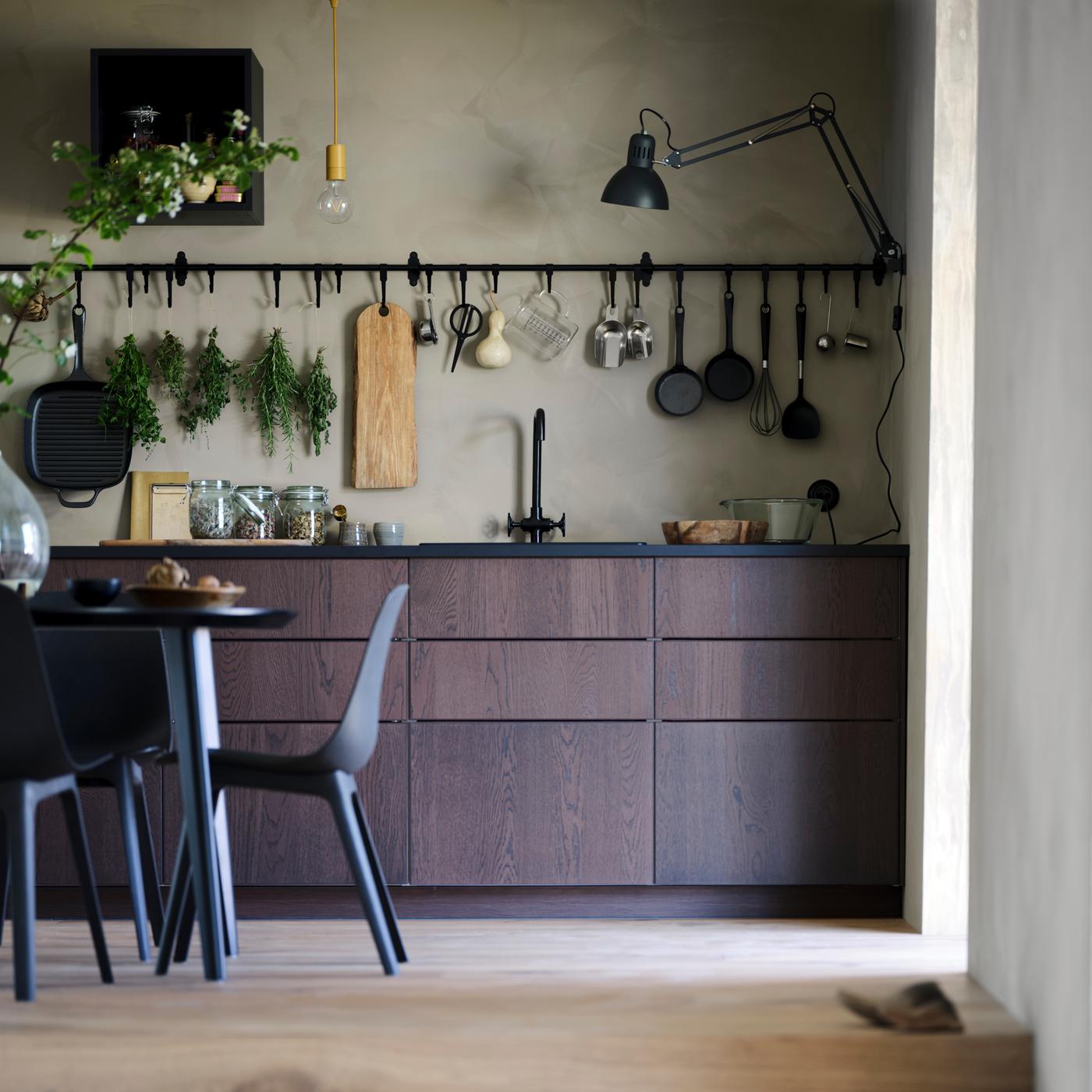 Cozinha SINARP em castanho com mesa em preto e cadeiras em antracite, calhas HULTARP em preto com artigos de cozinha em ganchos.