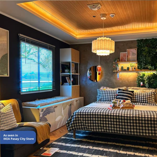 Cozy bedroom scene with a bed featuring a black and white checkered duvet, warm lighting, green plants, and wooden decor, creating a welcoming ambiance.