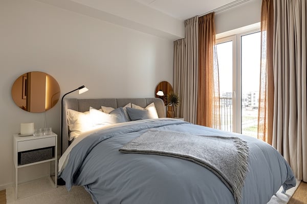 Cozy bedroom with upholstered bed, blue bedding, and natural light from large windows.